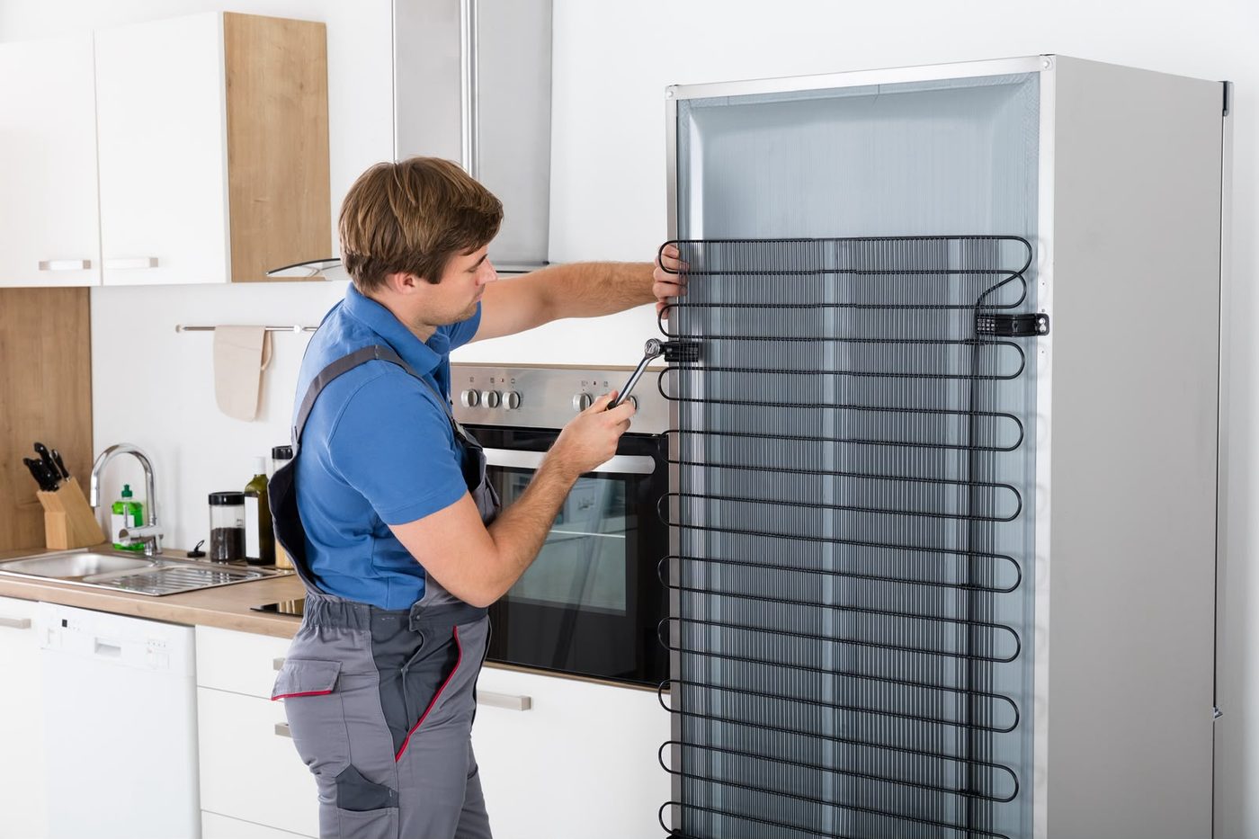 Technician cleaning the condenser coils at the back of a fridge